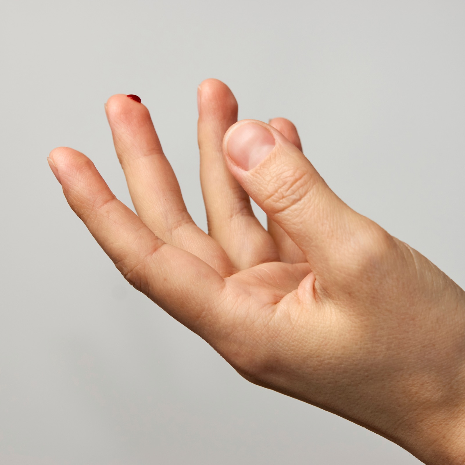 An open hand with a small blood drop on the fingertip — illustrating the fingerstick sample size